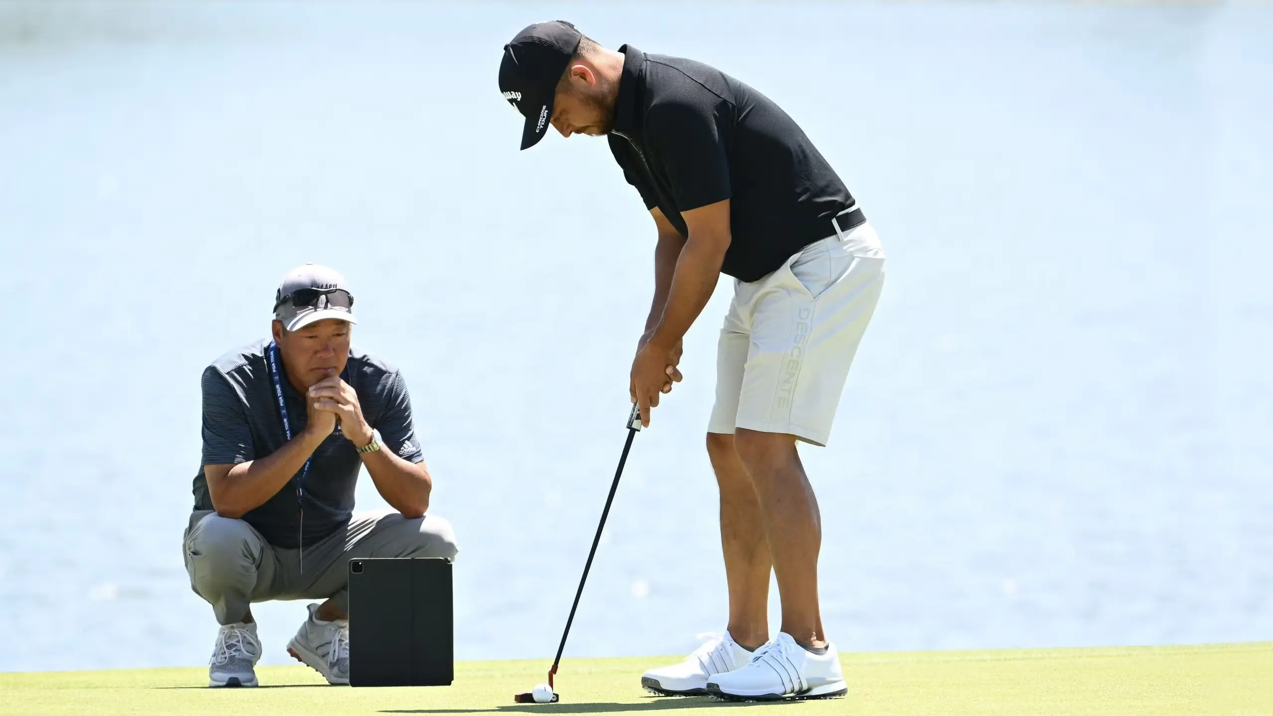 A golfer at dawn setting up to putt with a phone on a tripod recording from behind the ball