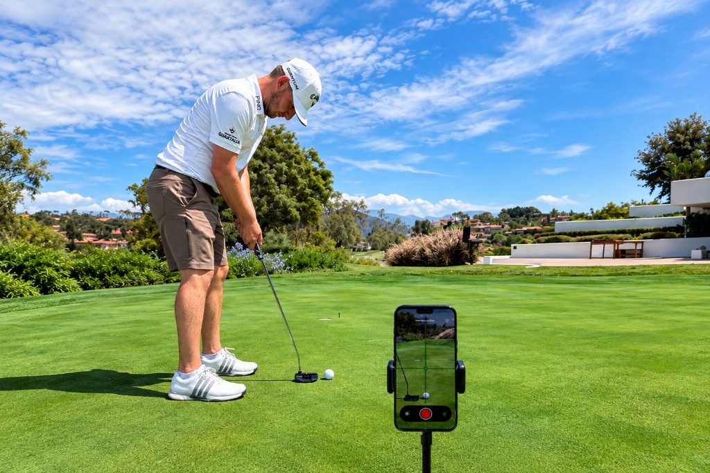 Golfer putting while Woosh records from a phone on a tripod behind the ball